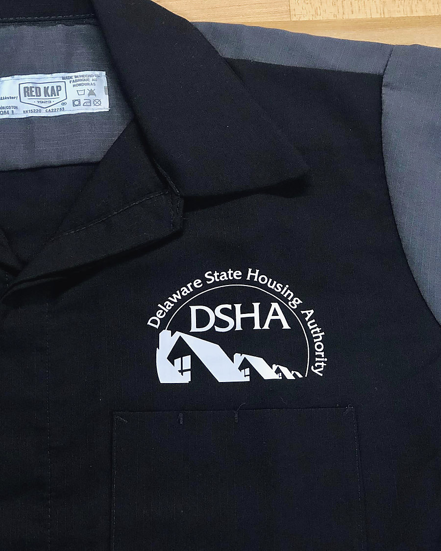 A black and grey work shirt with the Delaware State Housing Authority logo in white