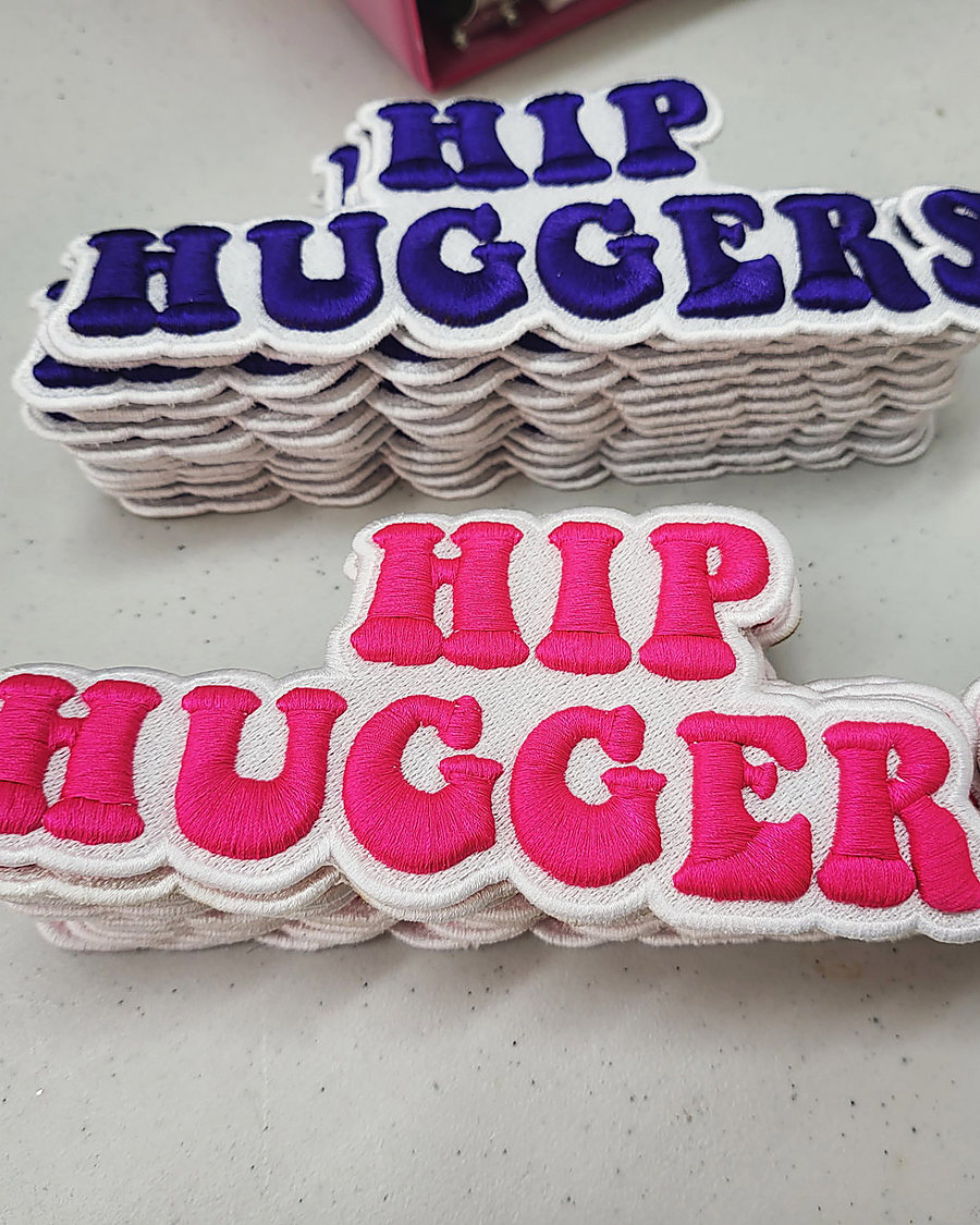 A stack of embroidered Hip Huggers patches in pink and purple