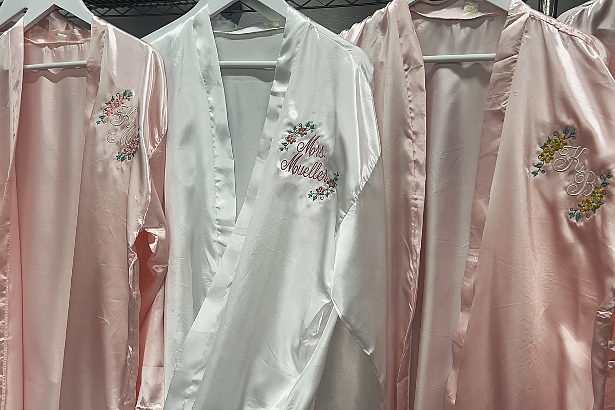Pink and white satin wedding robes on hangers, embroidered with a name and monograms among flowers